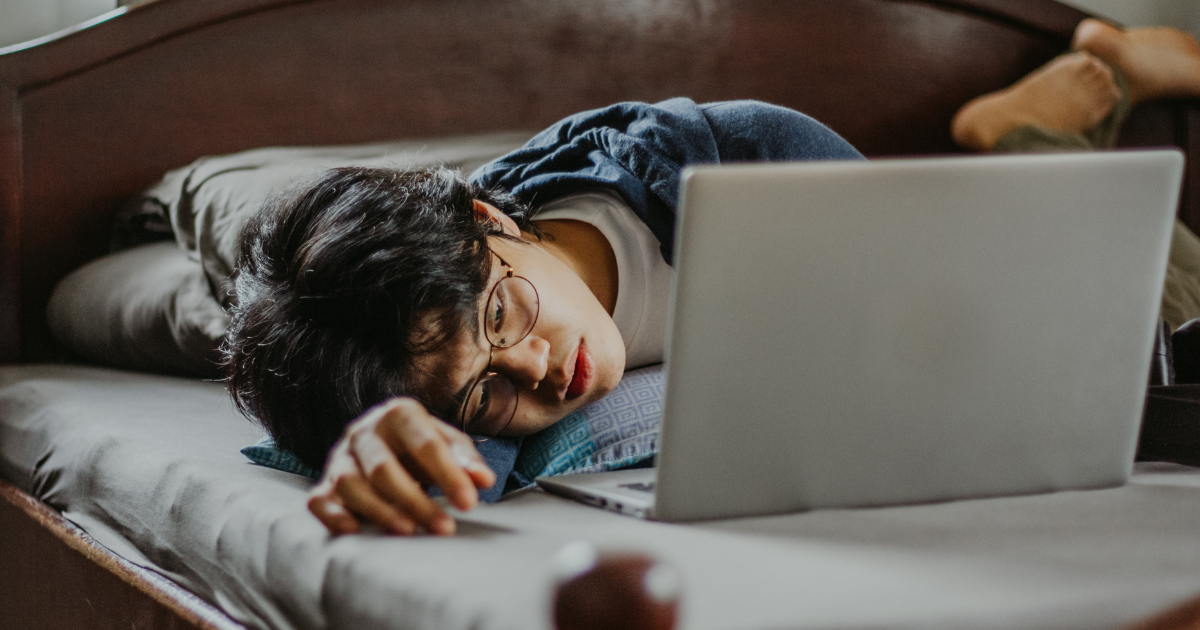 A tired student lying in bed looking at a laptop screen, illustrating the common fatigue and friction faced during a complex university online application.