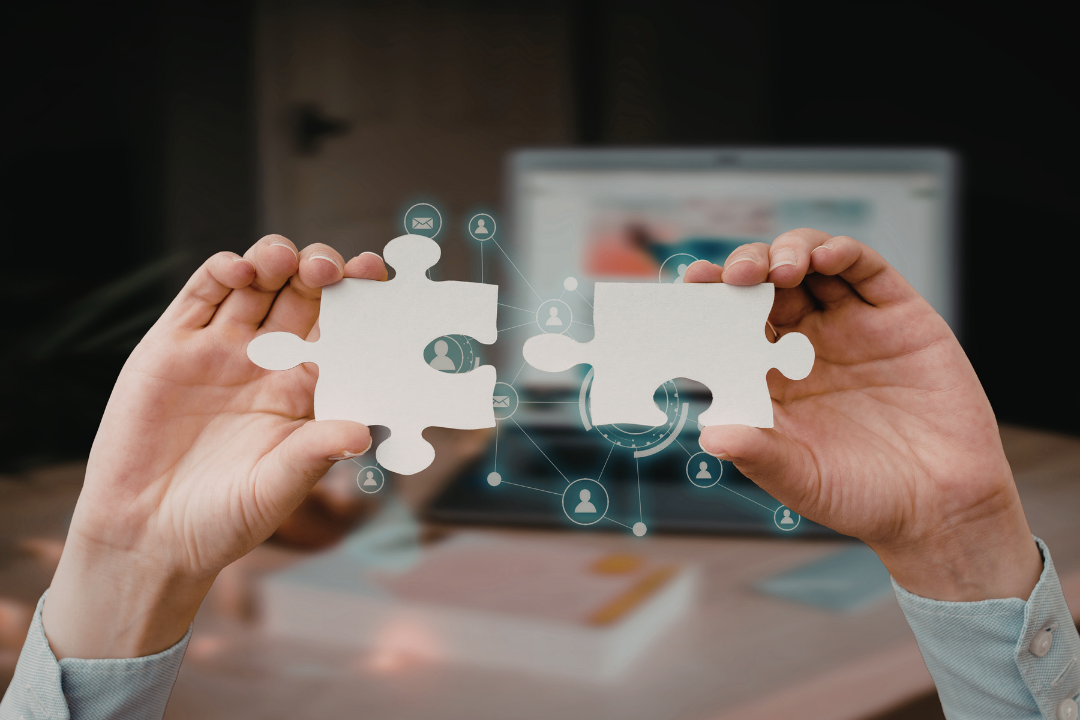 Two puzzle pieces being joined together in front of a laptop, representing a strategy to manage student data by connecting disparate institutional systems.
