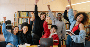 A group of diverse university students in a library celebrating, representing a successful strategy for attracting applicants to higher education institutions.
